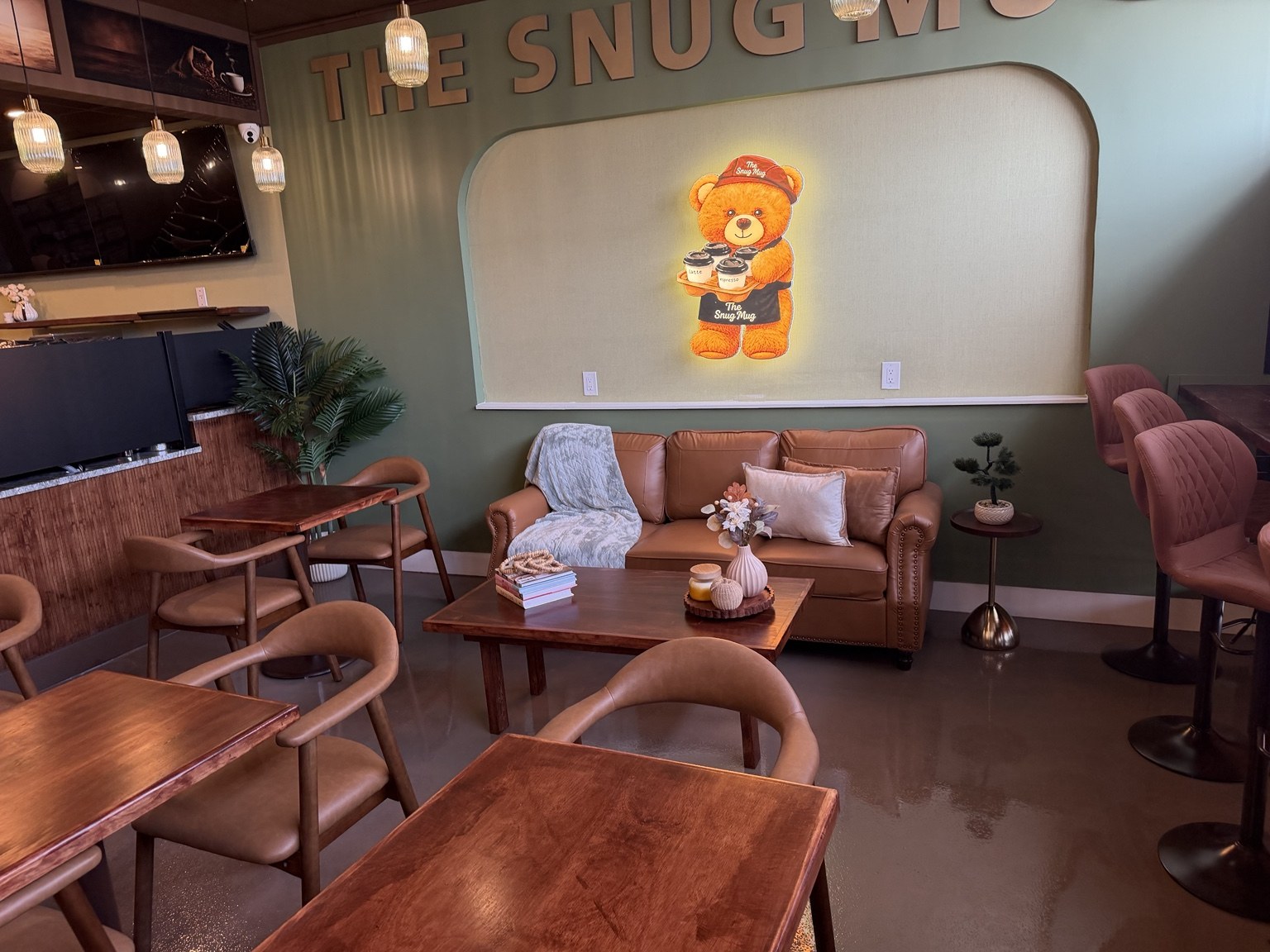 The Snug Mug seating area, with the illuminated bear mascot on the olive-green wall beneath the shop's wall lettering