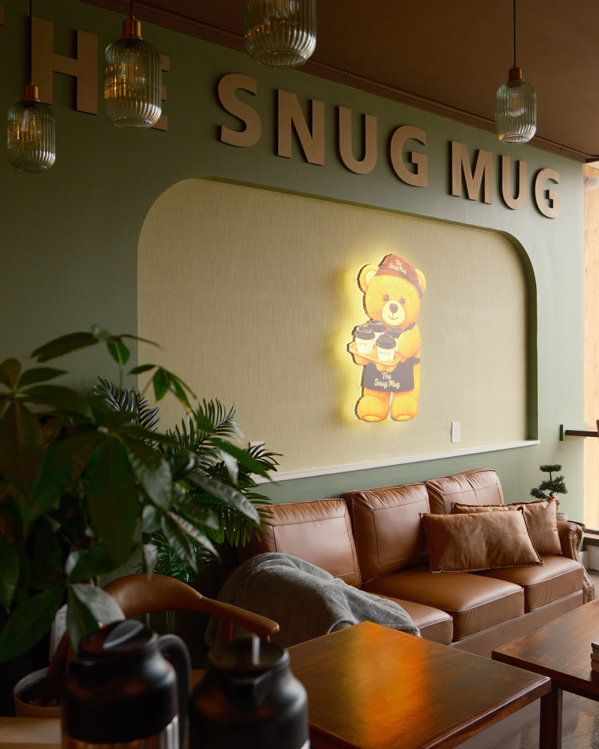 The Snug Mug lounge seen past a potted palm, the bear sign glowing on the wall