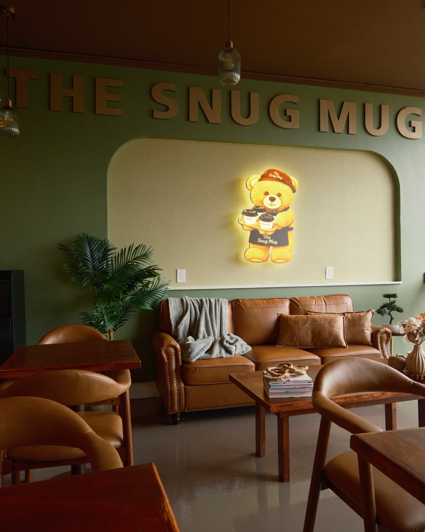 The lounge at The Snug Mug: leather sofa, olive wall, gold letters and the glowing bear sign